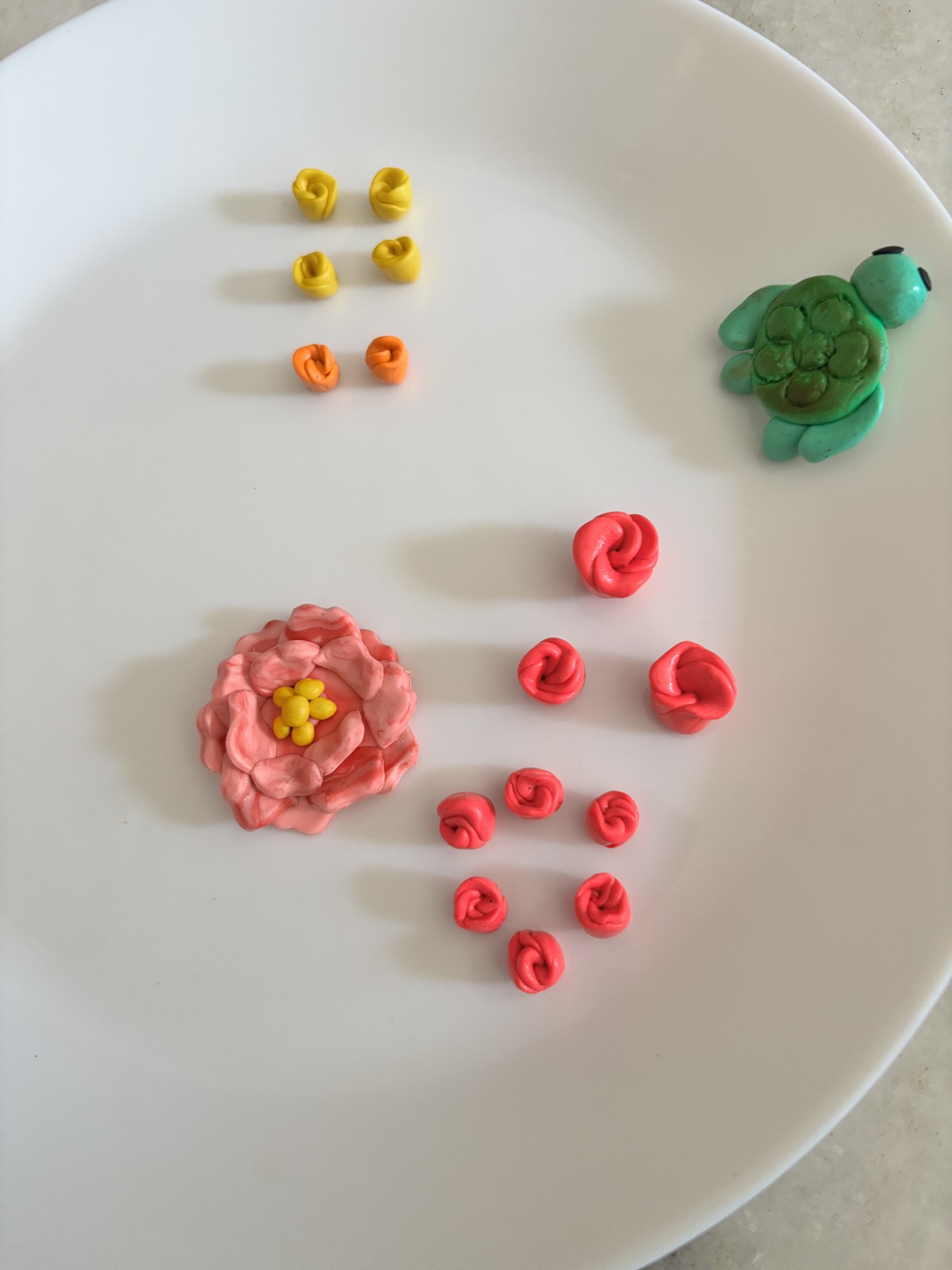 Small handmade clay flowers, rose shapes, and a green turtle arranged on a plate