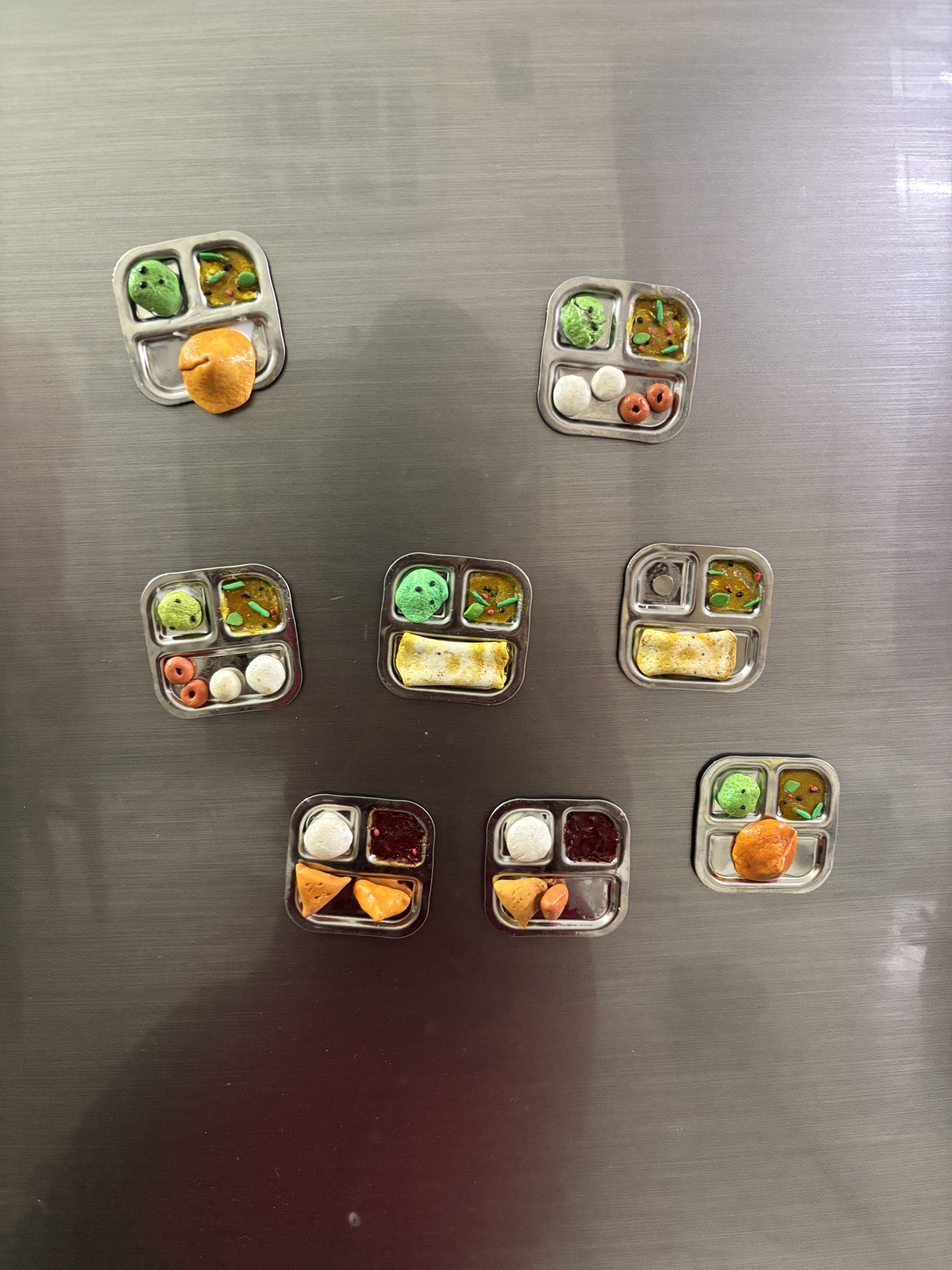 Miniature clay food trays displayed as magnets on a refrigerator