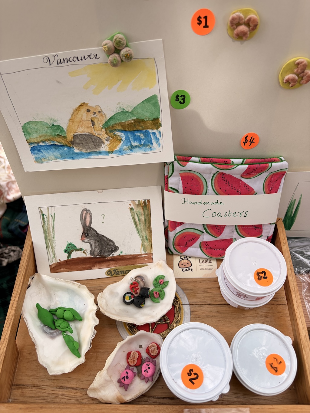 Watercolor paintings, handmade coasters, and little clay creations on a craft-sale table