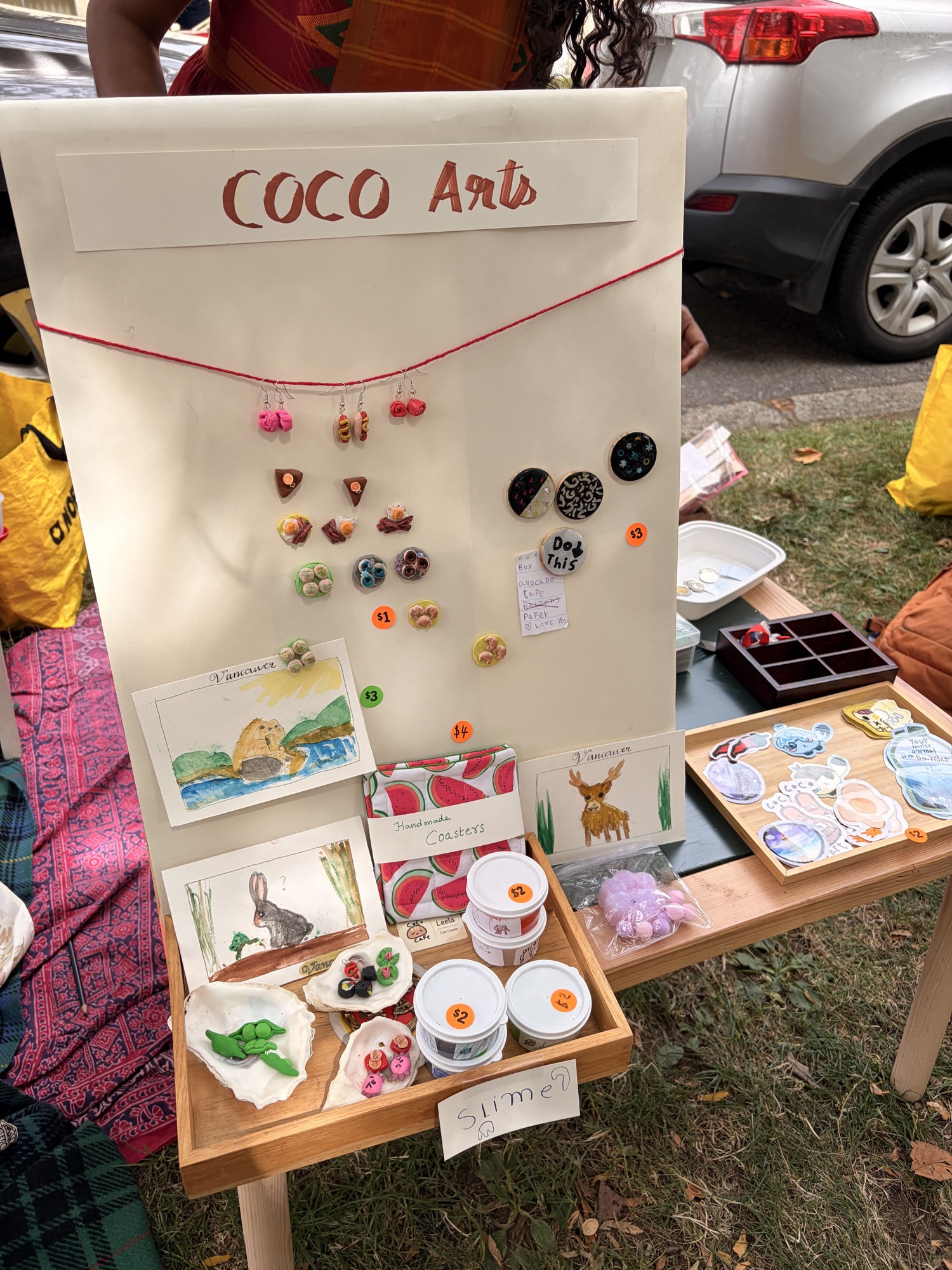 The full Coco Art craft-sale table with drawings, clay crafts, and stickers