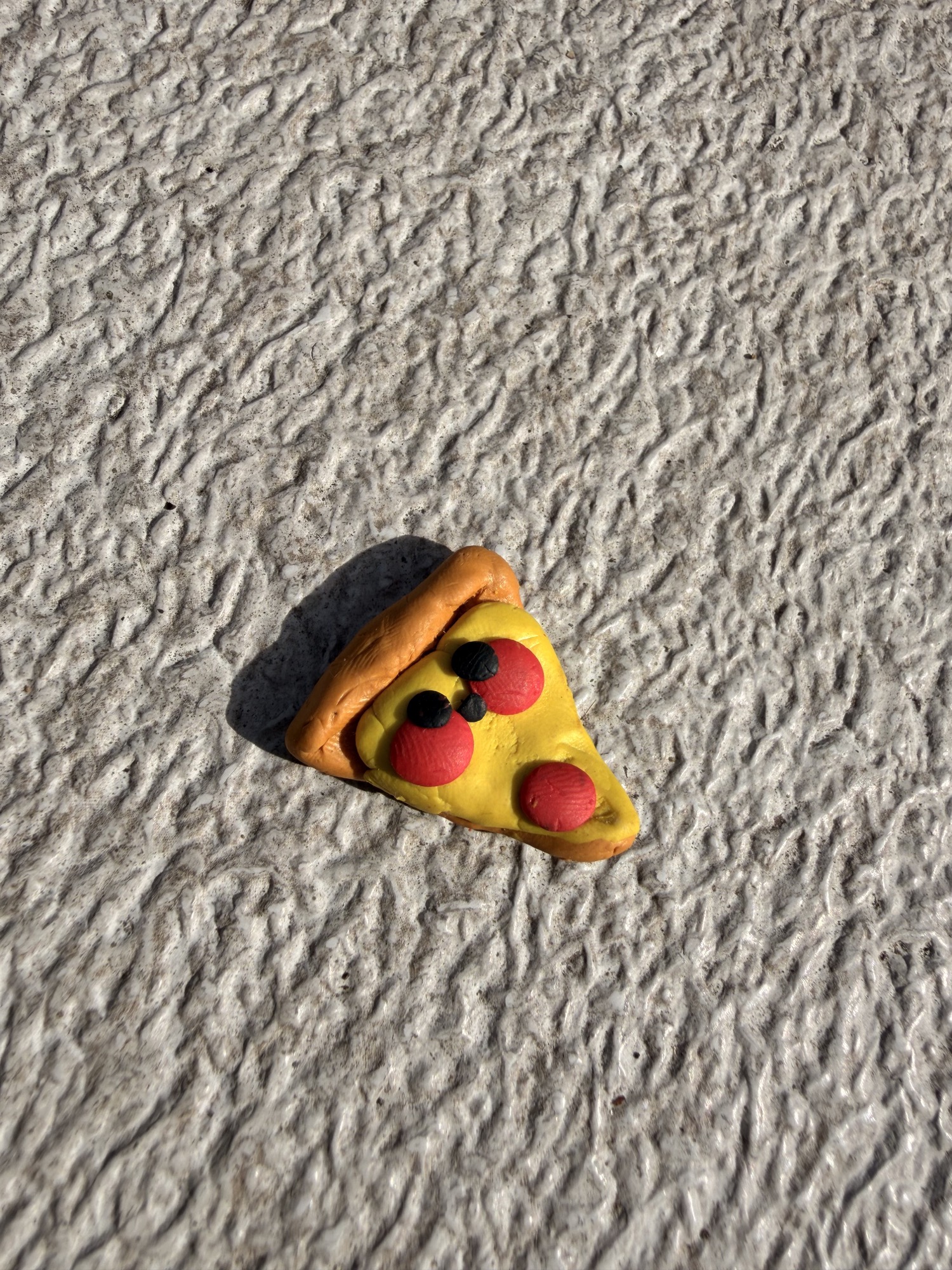 A miniature clay pizza slice with a smiling face